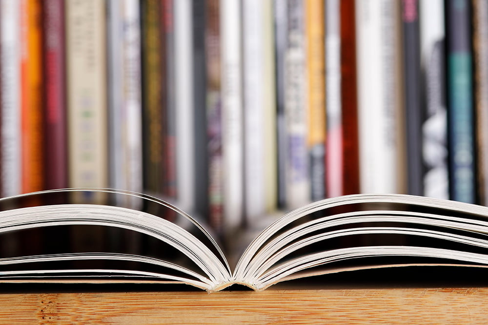 Close up of an open book against the backdrop of a shelf of books