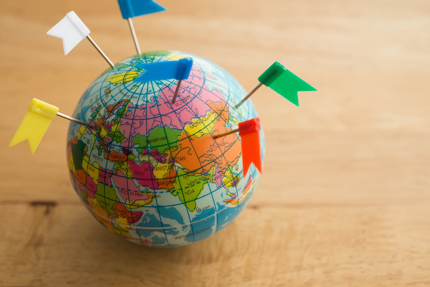 Color flag pins marks on earth globe with wooden table background.