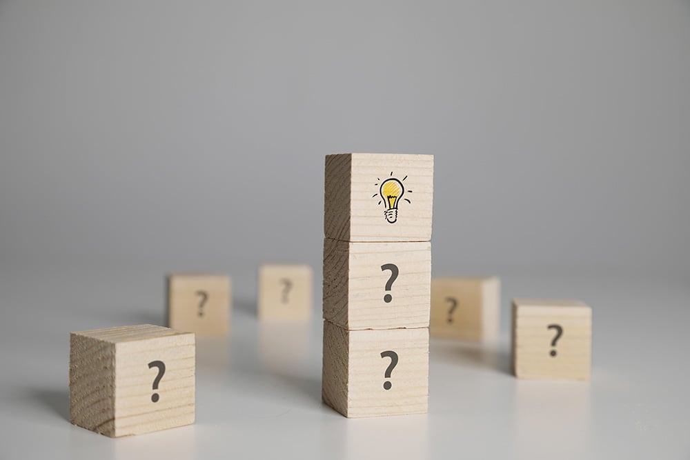 Wooden cubes with question marks, one stack topped with a light bulb icon.