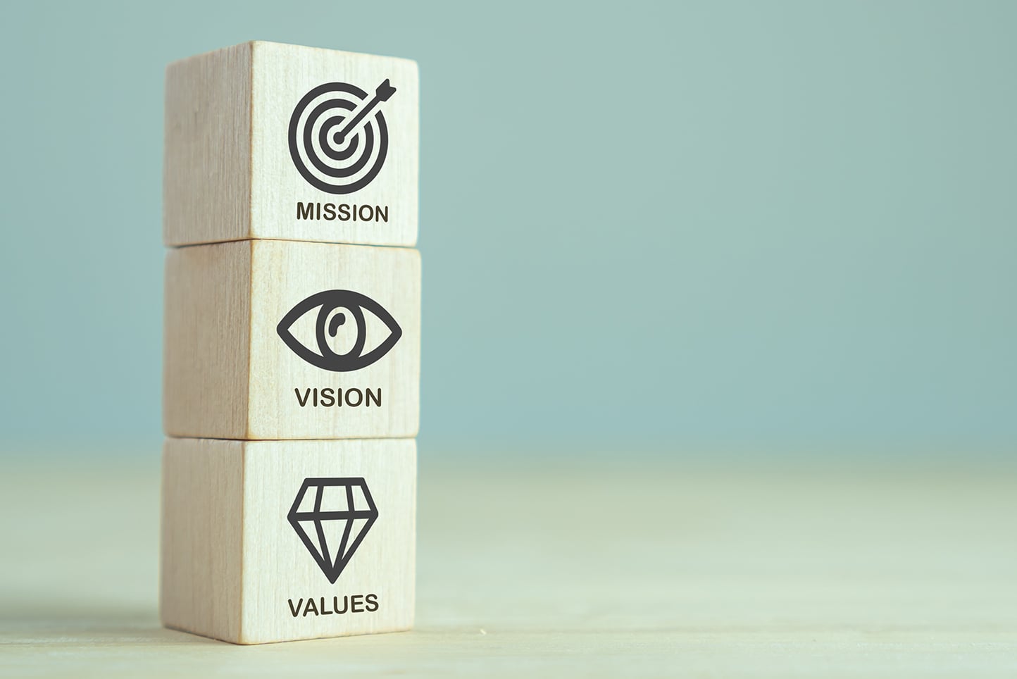 Stacked wooden blocks with symbols and words: mission, vision, values.